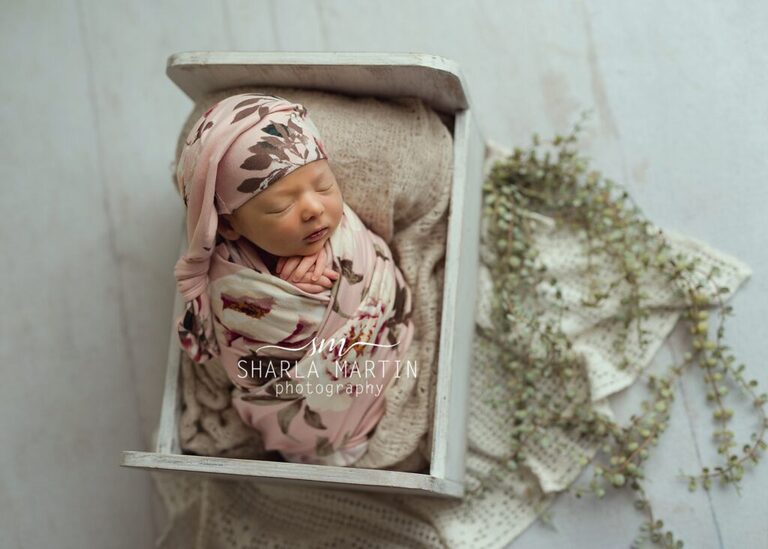 newborn baby posed in wooden bed with greenery