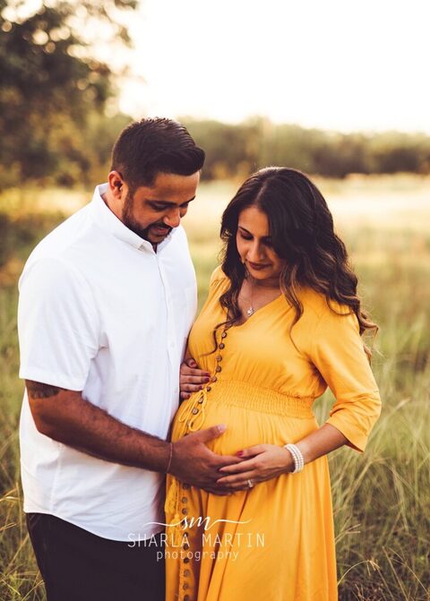 maternity couple looking at belly in field