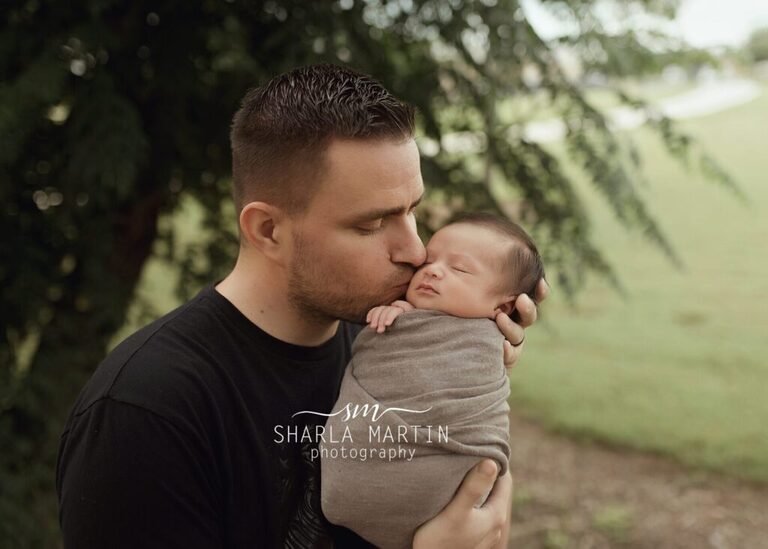 dad kissing baby boy outside for newborn photo shoot