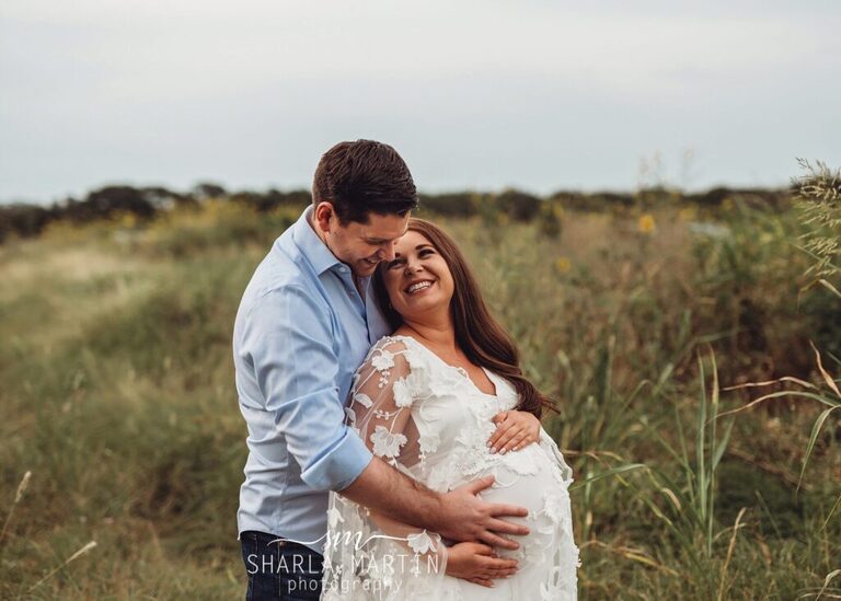 maternity photo shoot with couple smiling at each other in field