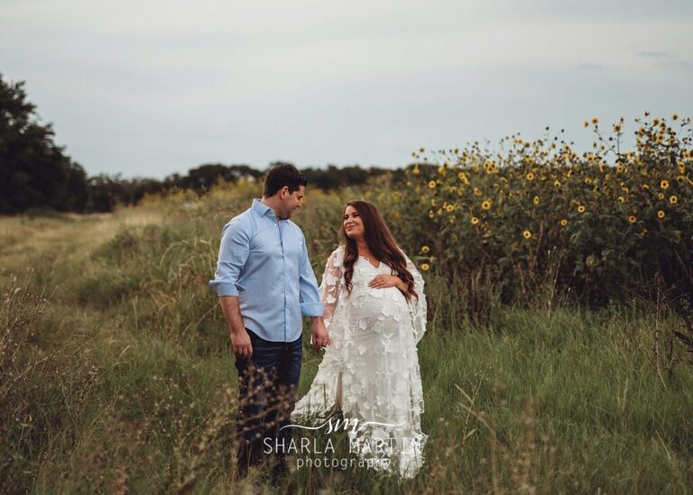 couple holding hands walking in sunflower field for maternity photography
