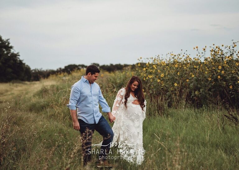 couple holding hands walking through field for maternity photo session austin