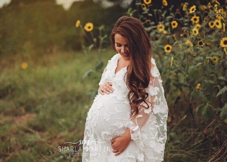 beautiful pregnant mother smiling at belly in sunflower field for maternity photos