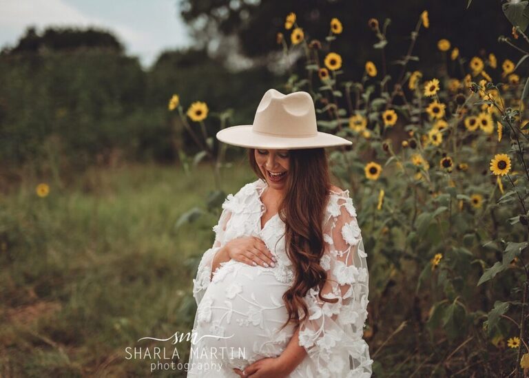 pregnant mother smiling at belly in sunflower field for maternity photos in austin