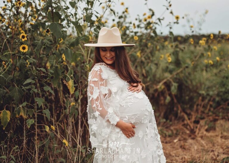 beautiful pregnant mother smiling at belly in sunflower field for maternity photos