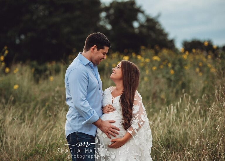 couple smiling at each other in field for maternity photo shoot in Austin