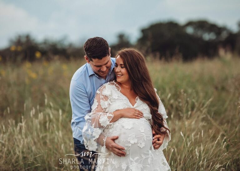 beautiful couple posing for maternity photos in field